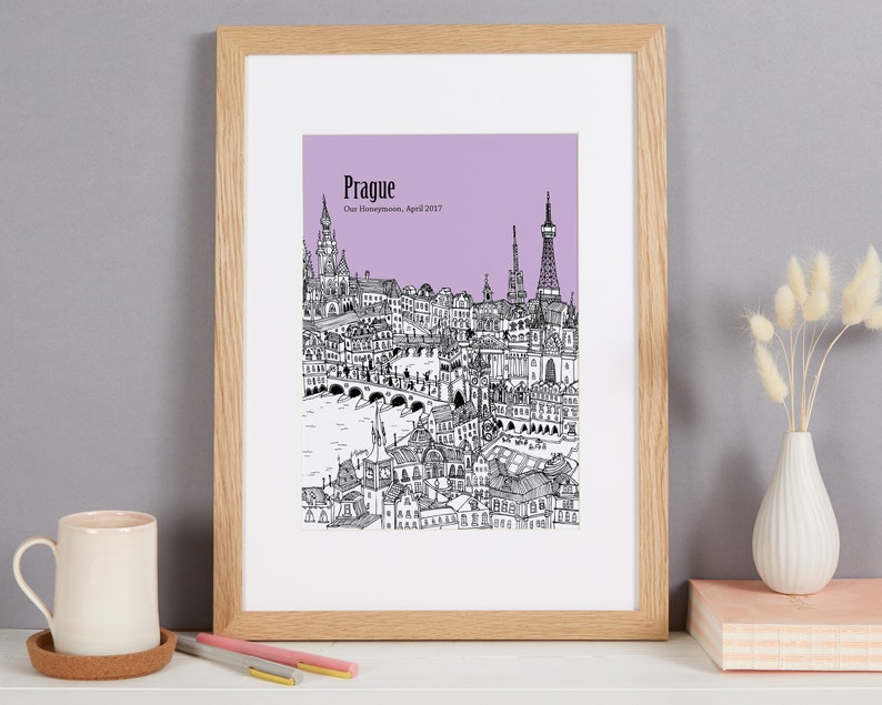 Op de afbeelding: Een zwart-witte lijntekening van de skyline van Praag op een lichtpaarse achtergrond. De tekst "Praag" en "Onze huwelijksreis, april 2017" staat onder de afbeelding.