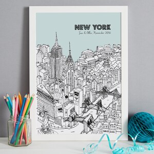 May include: A framed black and white illustration of the New York City skyline, including the Empire State Building, Chrysler Building, and Brooklyn Bridge. The text "NEW YORK" is at the top, with "Sue & Ollie, November 2016" below it. A jar of colored pencils sits to the left.