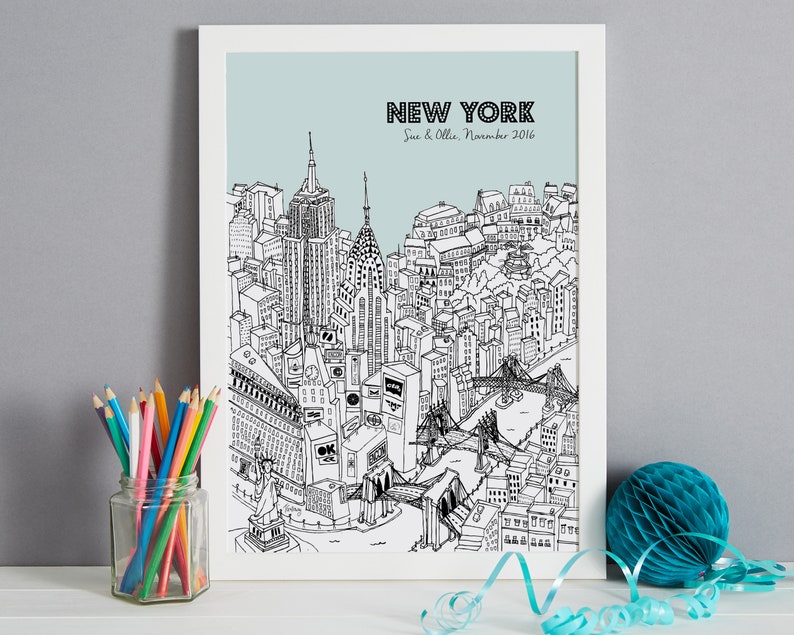 May include: A framed black and white illustration of the New York City skyline, including the Empire State Building, Chrysler Building, and Brooklyn Bridge. The text "NEW YORK" is at the top, with "Sue & Ollie, November 2016" below it. A jar of colored pencils sits to the left.