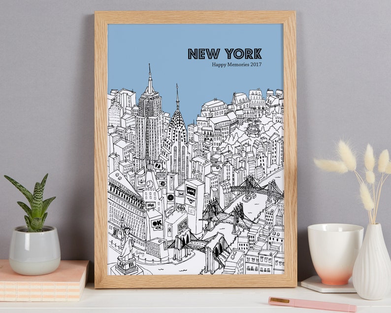 May include: A framed black and white illustration of New York City with a light blue sky background. The artwork includes iconic landmarks like the Empire State Building, Chrysler Building, and the Statue of Liberty. Text at the top reads "NEW YORK Happy Memories 2017".