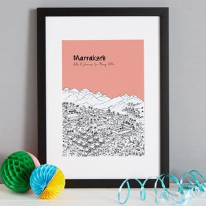 May include: A black framed print with a pink background and a black and white illustration of the city of Marrakech, Morocco. The text "Marrakech" and "Lila & James 1st May 2016" is printed in black on the pink background.