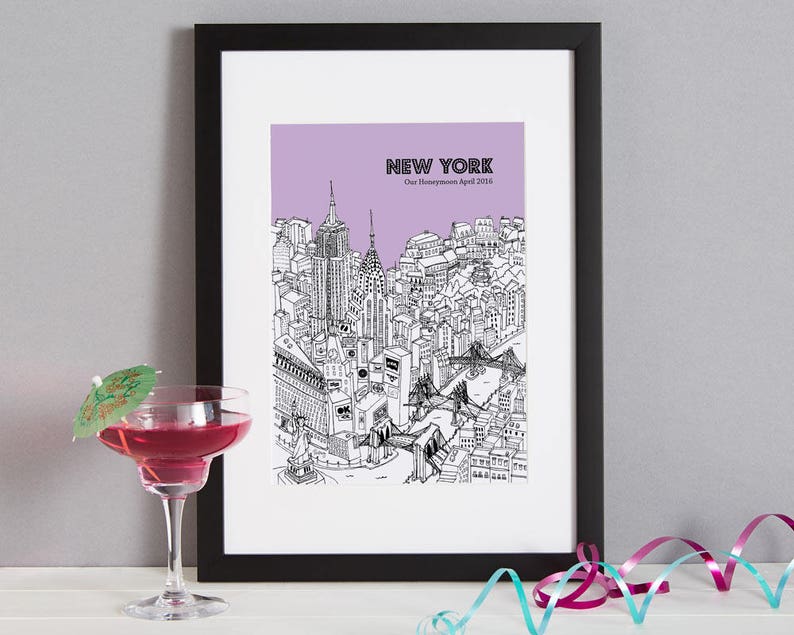 May include: Black framed print of a New York City skyline in black and white, with a purple background. The text "NEW YORK" and "Our Honeymoon April 2016" are visible. A cocktail with a green umbrella is in the foreground.