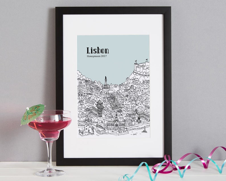 May include: A black framed print with a line drawing of Lisbon, Portugal. The print has a light blue background and the text "Lisbon Honeymoon 2017" is printed at the top.