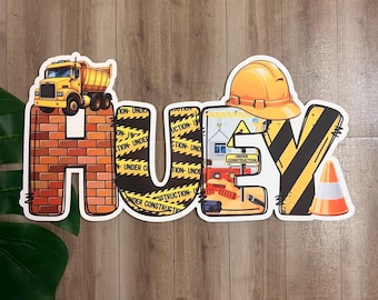 May include: A decorative sign spelling "HUEY" with construction-themed imagery. The "H" is a brick wall with a yellow dump truck. The "U" has caution tape, and the "E" features construction tools and a hard hat.