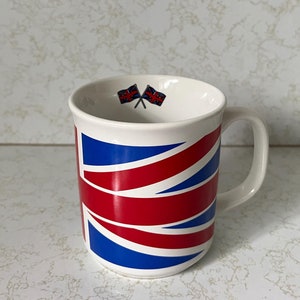 May include: White ceramic mug with a red, white, and blue Union Jack design. Two small crossed Union Jack flags are printed on the top of the mug.