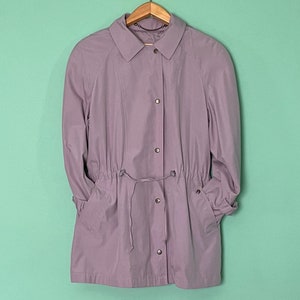 May include: A light purple jacket with a drawstring waist and long sleeves. The jacket has a collared neckline and button closure.