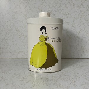 May include: A white metal tin with a yellow and brown illustration of a woman in a dress. The text on the tin reads "Cussons Poudre de Bain FOUGERE 400g. NET WT. 14 OZ. CUSSONS LONDON ENGLAND"