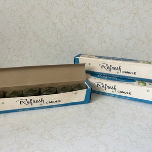May include: Two boxes of Refresh candles, each containing six green candles. The boxes are blue and white with the text "Refresh Candle" printed on them.