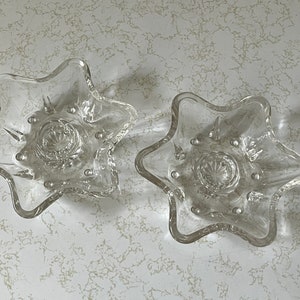 May include: Two clear glass star-shaped candle holders with a raised center and a beaded edge.