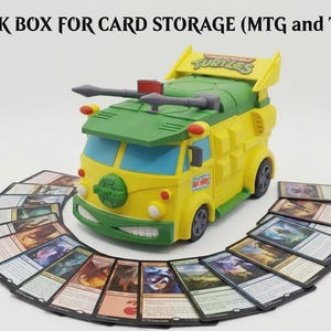 May include: A yellow and green Teenage Mutant Ninja Turtles party wagon deck box for card storage, featuring a roof-mounted weapon, a turtle shell emblem on the front, and a fan of assorted trading cards arranged in a semi-circle around the base.
