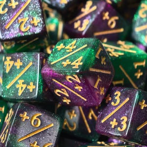 May include: Close-up of a collection of polyhedral dice in shades of green and purple with gold numbering. The dice are glittery and appear to be made of resin. The dice are used for tabletop games.