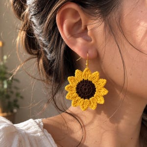 Peut inclure: Une boucle d'oreille en forme de tournesol réalisée en fil jaune et marron foncé. La fleur au crochet présente un centre circulaire marron foncé entouré de pétales jaunes pointus, suspendue à un crochet en métal doré pour oreilles percées.
