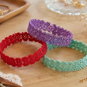 May include: Three circular bracelets made of delicate, interconnected floral lace patterns. The bracelets are colored in vibrant red, bright purple, and soft mint green. Each piece features a repeating scalloped edge design crafted from fine thread.