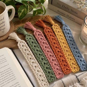 May include: A set of six rectangular crochet bookmarks in cream, sage green, dusty rose, burnt orange, mustard yellow, and light blue. Each bookmark features a repeating star-like stitch pattern and a small tassel at the top end.