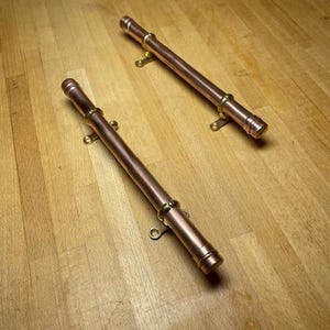 Peut inclure: Deux poignées de tiroir en cuivre avec des accents en laiton. Les poignées mesurent environ 25 cm de long et ont une extrémité arrondie.