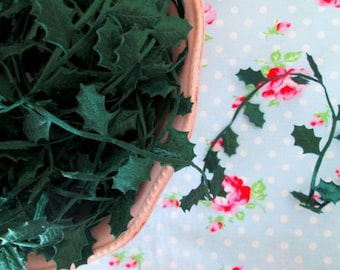 May include: A bowl filled with dark green velvet holly leaves. The leaves are arranged in a random pattern and are perfect for crafting or decorating.