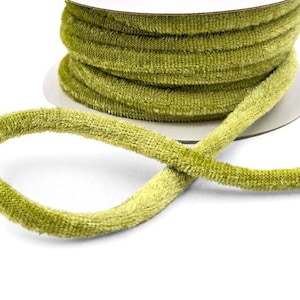 May include: A spool of olive green velvet ribbon. The ribbon is round and has a soft, textured appearance. The spool is white and the ribbon is unwound, creating a loop.