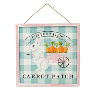 May include: A square wooden sign with a pink frame and a rope for hanging. The sign features a white bunny pulling a cart of carrots. Text reads "Cottontail's Carrot Patch" on a blue and white checkered background.
