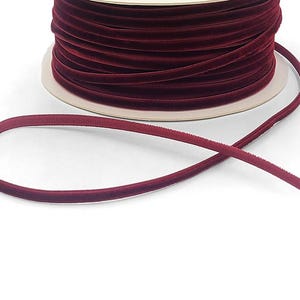 May include: A spool of burgundy velvet ribbon. The ribbon is thin and has a smooth, soft texture.