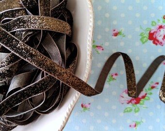 May include: A close-up of a spool of brown velvet ribbon with gold glitter. The ribbon is in a white bowl and is on a blue and white polka dot fabric.