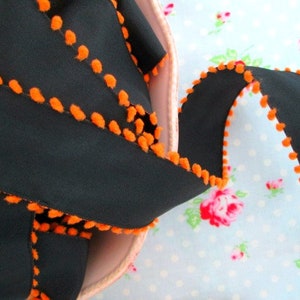 May include: Black ribbon trim with orange pom poms. The ribbon is in a bowl and the pom poms are on the edge of the ribbon.