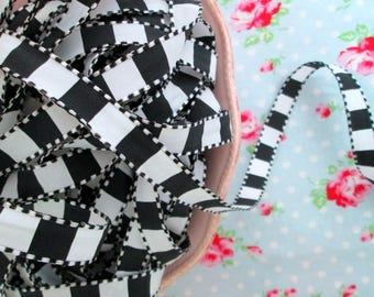 Puede incluir: Cinta a cuadros negros y blancos con un borde blanco en zigzag. La cinta está en un cuenco y se derrama sobre una superficie con estampado azul y blanco.