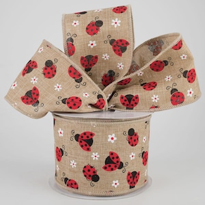 May include: A roll of tan burlap ribbon featuring a repeating pattern of red ladybugs with black spots and white daisy flowers. The ribbon is arranged in a decorative bow, perfect for crafts and seasonal decor.
