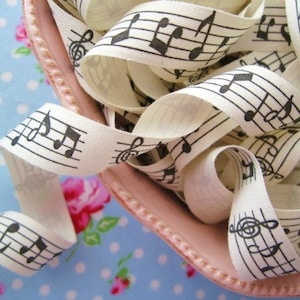 May include: White cotton ribbon with black musical notes printed on it. The ribbon is rolled up and piled on top of itself.