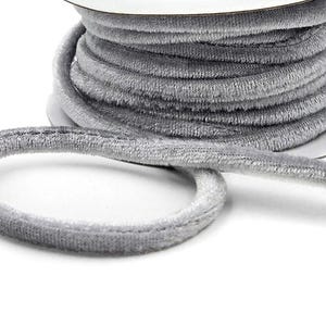 May include: A spool of gray velvet ribbon. The ribbon is round and has a soft, fuzzy texture. The spool is white and the ribbon is coiled around it. The ribbon is unraveled in a loop.