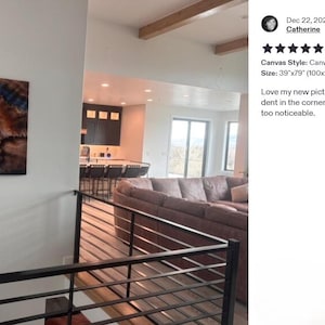 a modern living room with a large abstract painting on the wall, a comfortable couch, and a kitchen visible in the background.