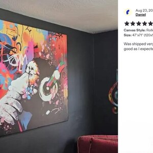 a large, colorful abstract painting hanging on a wall. The painting is vibrant and eye-catching, with a mix of bold colors and dynamic brushstrokes. The wall on which the painting is mounted is black, providing a striking contrast to the artwork. The painting appears to be a modern, contemporary piece that adds a lively and energetic atmosphere to the room.