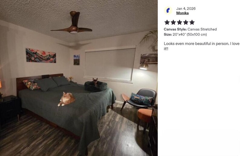 a bedroom with a large bed, a cat resting on the bed, and a painting on the wall. The room has a wooden ceiling fan and a window with a white curtain.
