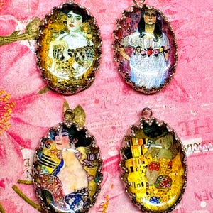 May include: Four oval-shaped pendants featuring artistic portraits and figures in a metallic scalloped setting. Each pendant displays a distinct colorful illustration with gold, yellow, blue, and floral tones, topped with a small silver loop.