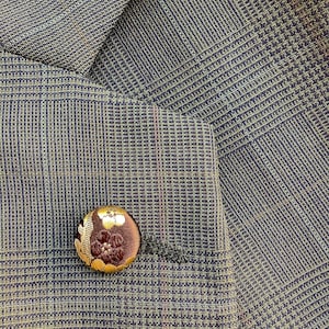 May include: A brown button with a gold floral pattern on a plaid fabric background.
