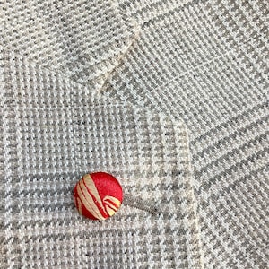 May include: A red button with gold accents and a swirling pattern on a beige fabric background.