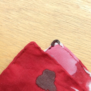 May include: Close-up of two fabric squares with a floral pattern. One square is primarily red with a dark brown splotch, while the other is pink with white and dark accents. The squares are on a light brown wooden surface.