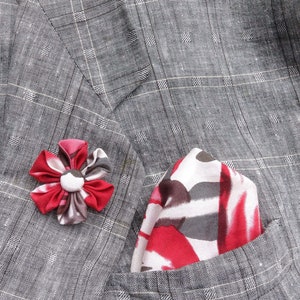 May include: A gray plaid blazer with a red, white, and gray patterned pocket square and a red and gray flower lapel pin. The blazer has a classic design and is made of a textured fabric.