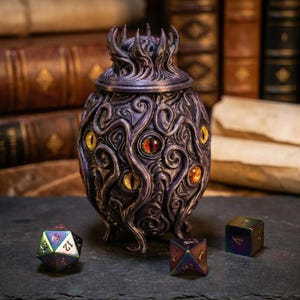 May include: A detailed, purple fantasy jar with a lid, decorated with multiple yellow and red eye designs. Three iridescent dice are placed near the jar, suggesting a tabletop gaming theme. The jar has a textured surface and a unique, tentacle-like design.