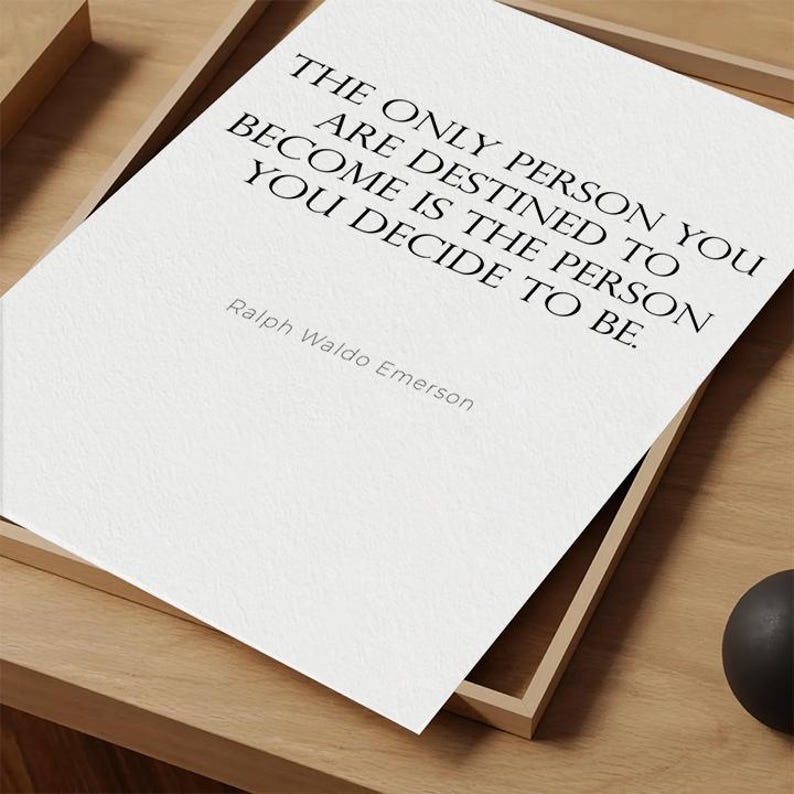 K&ouml;nnte beinhalten: Gerahmter Druck mit dem Zitat &bdquo;THE ONLY PERSON YOU ARE DESTINED TO BECOME IS THE PERSON YOU DECIDE TO BE.&ldquo; von Ralph Waldo Emerson. Der schwarze Text befindet sich auf wei&szlig;em Hintergrund in einem Holzrahmen.