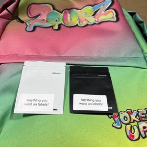 May include: A pink, green and blue gradient backpack with the word "ZURZ" printed in rainbow colours. Two resealable bags are attached to the front of the backpack, one white and one black. Both bags have the text "Anything you want on labels!" printed on them.