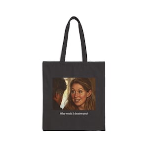 Puede incluir: Un bolso tote negro con un estampado gráfico rectangular de una persona con cabello largo castaño mirando a otro individuo. Debajo de la imagen, el texto "Why would I deceive you?" está impreso en blanco sobre la superficie de tela negra.