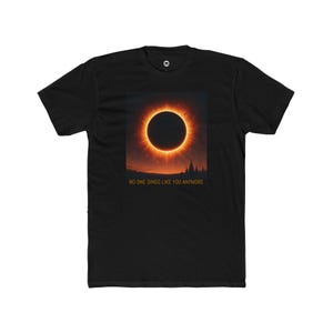 May include: Black t-shirt featuring a vibrant graphic of a solar eclipse with a fiery orange corona. The text "NO ONE SINGS LIKE YOU ANYMORE" is printed below the image. A stylish tee for those who appreciate unique designs.