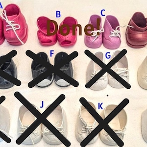 May include: A collection of doll shoes labelled A through L, with some marked with black X symbols. The available pairs include bright pink lace-up trainers, pink open-toe shoes, light pink lace-up trainers, dark pink loafers, and off-white textured trainers.