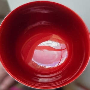 May include: A circular bowl with a smooth, vibrant red interior surface. The bowl features a deep, rounded basin with a glossy finish that reflects light, creating a bright highlight in the center. The rim is perfectly round and uniform.