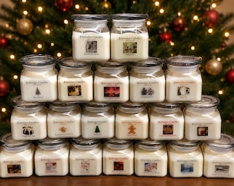 May include: A collection of glass jar candles with lids, arranged in a pyramid shape. Each candle has a label with the text "Kittredge Candles" and a unique image. The background features a Christmas tree with ornaments and lights.