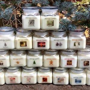 May include: A pyramid display of 18 glass jar candles with white lids. Each candle has a different image on the front, including a Christmas tree, a gingerbread man, and a pine cone. The candles are labeled "Kittredge Candles".