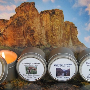 May include: Four silver candle tins with labels featuring images and text. The labels read "Kittredge Candles 100% Pure Soy Candle" and feature images of Idaho Potatoes, Western White Pine, Hell's Canyon, and Priest Lake Huckleberries.