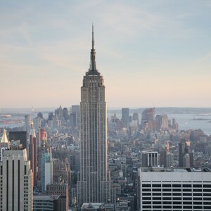 May include: An aerial view of the New York City skyline, dominated by the Empire State Building. The iconic skyscraper stands tall amidst other buildings, with a soft, natural light illuminating the scene. The image captures the urban landscape.