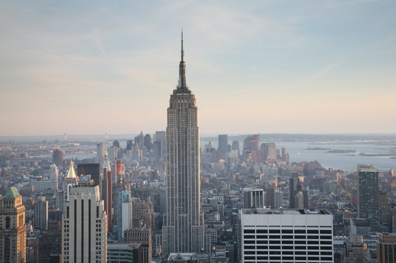 May include: An aerial view of the New York City skyline, dominated by the Empire State Building. The iconic skyscraper stands tall amidst other buildings, with a soft, natural light illuminating the scene. The image captures the urban landscape.