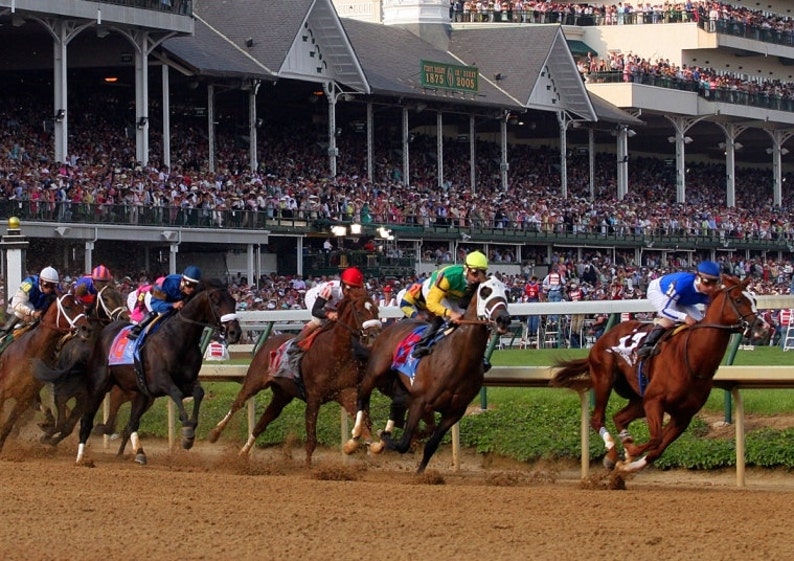 May include: A horse race in progress, with several horses and jockeys competing on a dirt track. The jockeys wear colorful silks, and a large crowd watches from the stands. The scene is set at a racetrack with a grandstand.